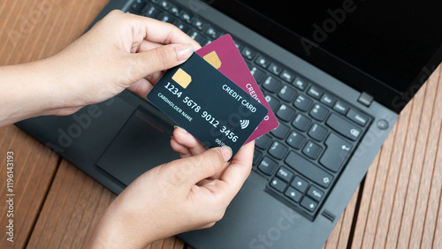 Hand holding a red and black credit card with laptop