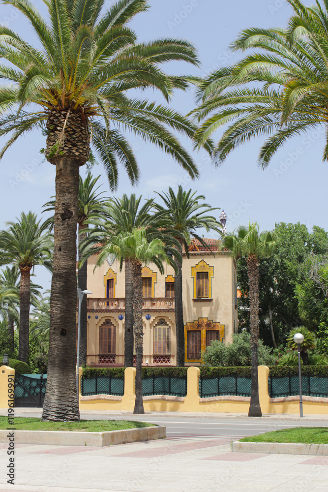 Beautiful palm-lined street in Salou, Spain featuring a charming historical building and vibrant greenery Beautiful palm-lined street in Salou, Spain featuring a charming historical building and vibrant greenery