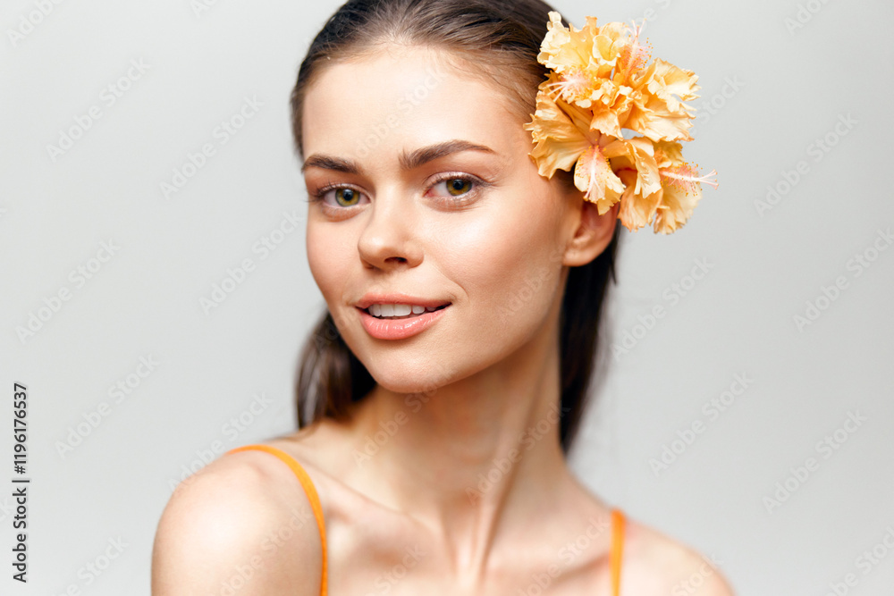 Young woman with flower in hair, smiling gently, wearing orange outfit, against soft gray background, exuding warmth and positivity, summer vibes. Young woman with flower in hair, smiling gently, wearing orange outfit, against soft gray background, exuding warmth and positivity, summer vibes.