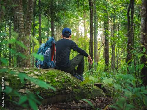 Solo hiker takes break to drink water while sitting on fallen tree in lush rainforest at Phu Soi Dao National Park, Thailand. photo