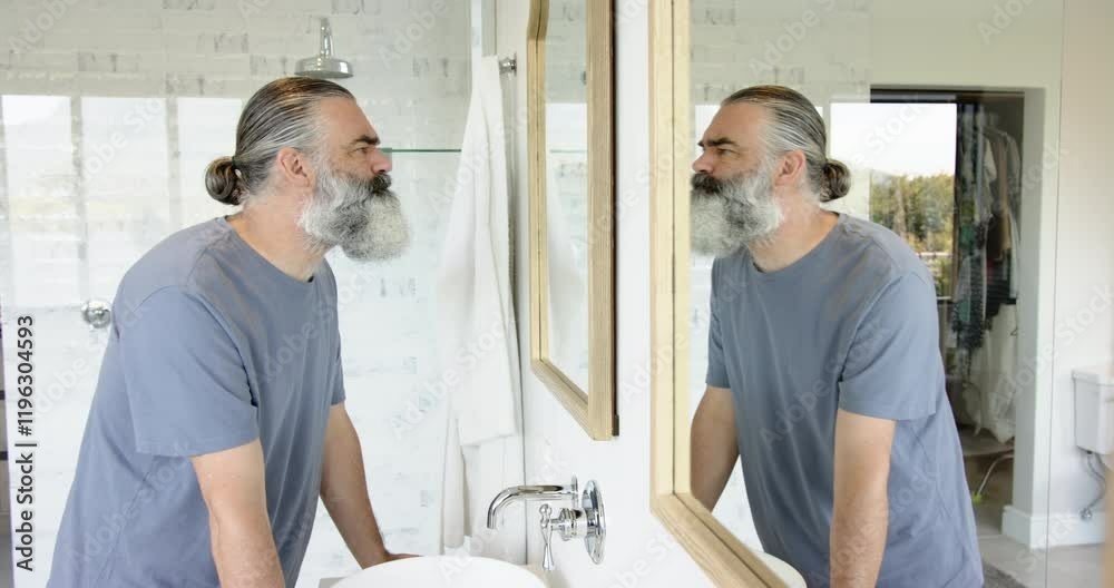Man with gray beard looking at reflection in bathroom mirror, appearing thoughtful Man with gray beard looking at reflection in bathroom mirror, appearing thoughtful
