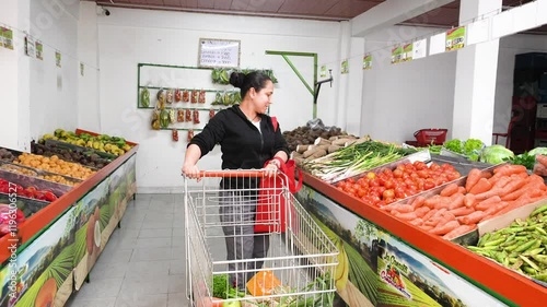 A young woman is choosing tomatoes to buy and take home in a supermarket with various fruits and vegetables
