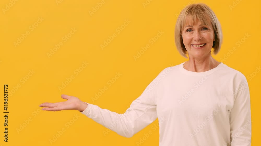 A smiling woman in a white top extends her arm with an open hand, showcasing an inviting gesture. The vibrant yellow backdrop enhances her warm demeanor and cheerful expression, copy space