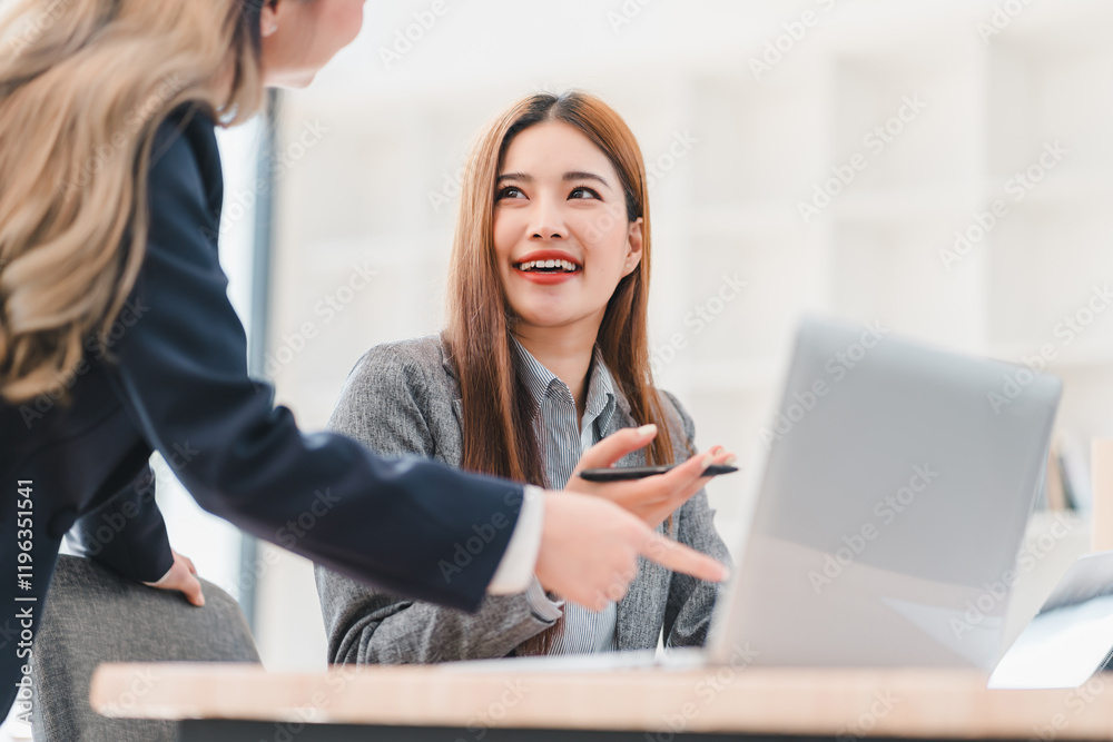 Cheerful businesswoman in gray blazer discusses work with colleague while using laptop in bright modern office setting Cheerful businesswoman in gray blazer discusses work with colleague while using laptop in bright modern office setting