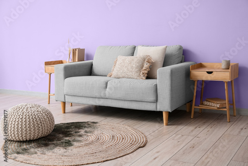 Comfortable sofa and tables near violet wall in room interior photo