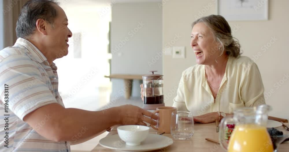 Enjoying breakfast, senior couple smiling and toasting with coffee mugs at table Enjoying breakfast, senior couple smiling and toasting with coffee mugs at table