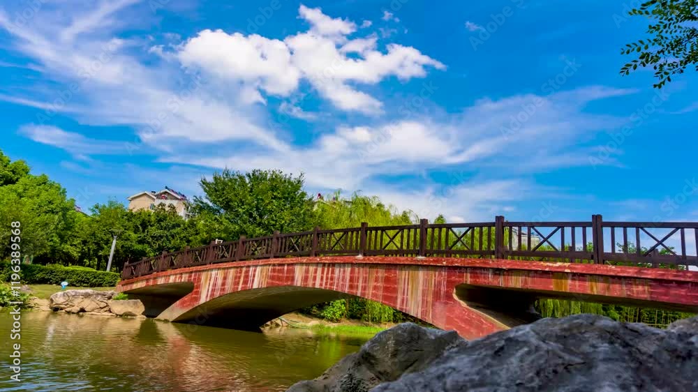 Beautiful summer time lapse of a bridge in a park under a blue sky with fluffy clouds Beautiful summer time lapse of a bridge in a park under a blue sky with fluffy clouds