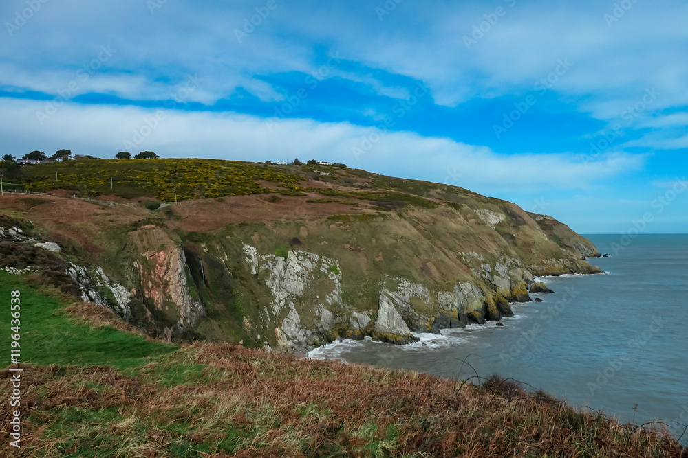 Rugged coastline in Howth, Dublin, Ireland under grey overcast sky. Steep cliffs covered in dry vegetation drop down to choppy Atlantic Ocean. Wild windswept beauty. Peaceful solitude, coastal beauty Rugged coastline in Howth, Dublin, Ireland under grey overcast sky. Steep cliffs covered in dry vegetation drop down to choppy Atlantic Ocean. Wild windswept beauty. Peaceful solitude, coastal beauty
