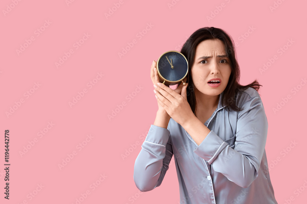 Stressed young woman in pajamas with alarm clock on pink background Stressed young woman in pajamas with alarm clock on pink background