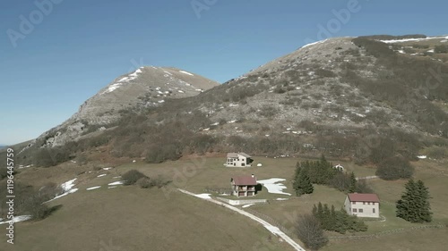 Drone view over Valsorda, Gualdo Tadino, on a sunny winter day. Snow-dusted peaks rise above a vibrant landscape, blending crisp white and rich earthy tones under a clear blue sky photo