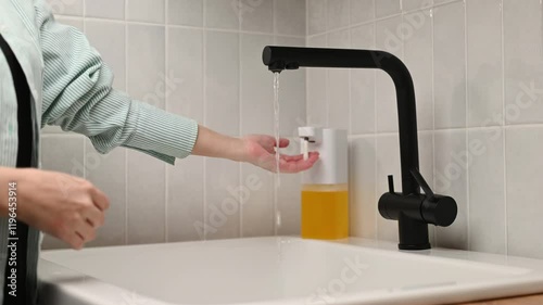 An unrecognizable woman washes her hands with soap suds from a dispenser in the home room. Hand hygiene.