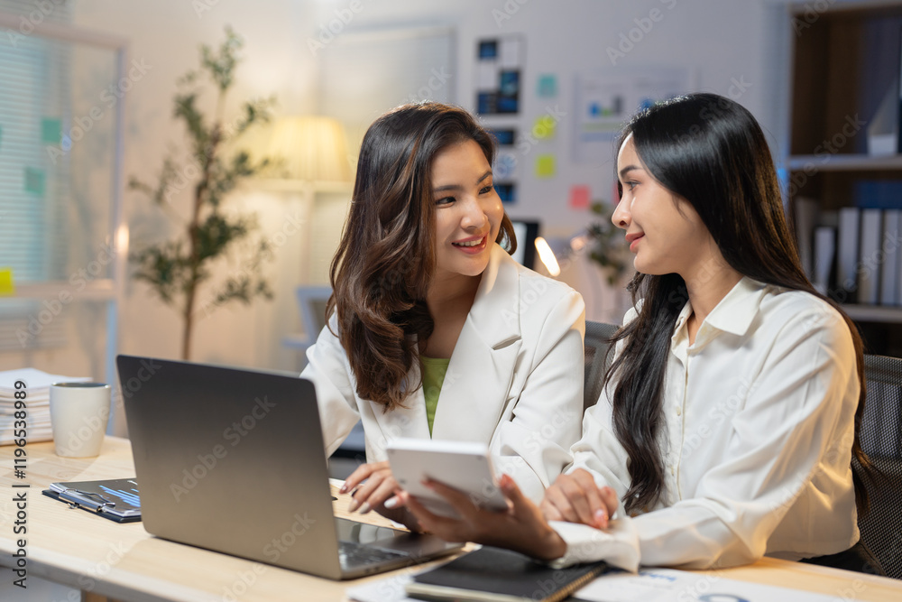 Two young asian businesswomen are using a laptop and calculator, working together on a project in a modern office, collaborating effectively and displaying teamwork Two young asian businesswomen are using a laptop and calculator, working together on a project in a modern office, collaborating effectively and displaying teamwork