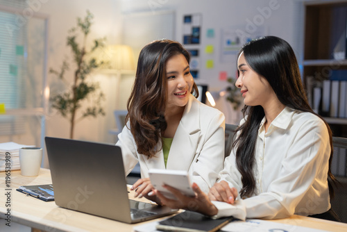 Two young asian businesswomen are using a laptop and calculator, working together on a project in a modern office, collaborating effectively and displaying teamwork