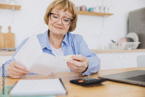 Senior business woman holding paper bill using calculator, old lady managing account finance, calculating money budget tax, planning banking loan debt pension payment sit at home kitchen table.