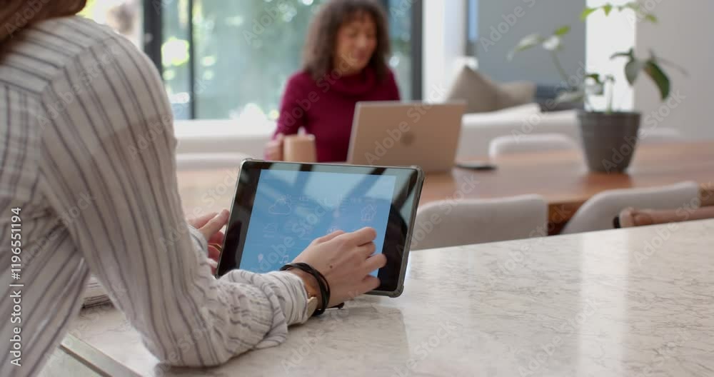 Using tablet for home automation, woman in background working on laptop Using tablet for home automation, woman in background working on laptop