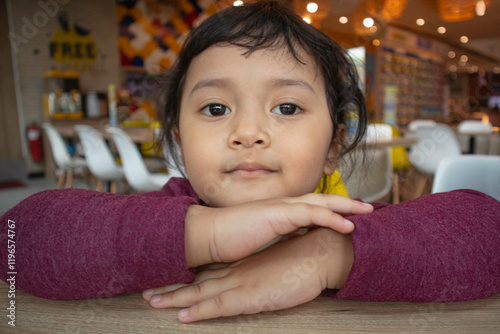 Smiling toddler girl with serious face resting on folded hands