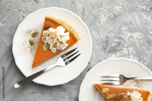 Pieces of tasty homemade pumpkin pie with whipped cream and seeds on grey table, top view photo