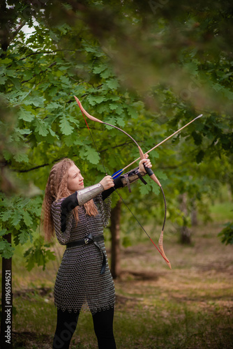 A young woman warrior with wavy hair and in chain mail armor holds a bow with arrows in her hands. photo