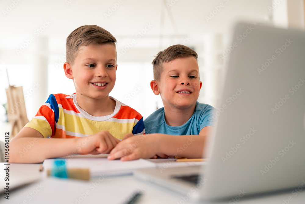Two Caucasian boys in casual attire collaborate on schoolwork at home, using laptop and writing materials for their educational activities. Two Caucasian boys in casual attire collaborate on schoolwork at home, using laptop and writing materials for their educational activities.