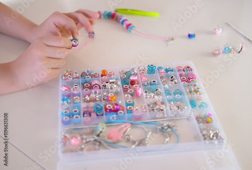 Fashion, creativity. Hobby concept. Сhild makes jewelry with his own hands, stringing colorful beads on thread. Selective focus.