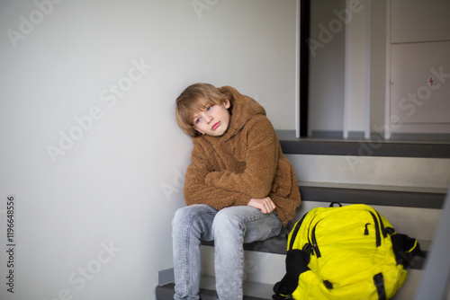 Sad boy sitting on school stairs with a backpack.
