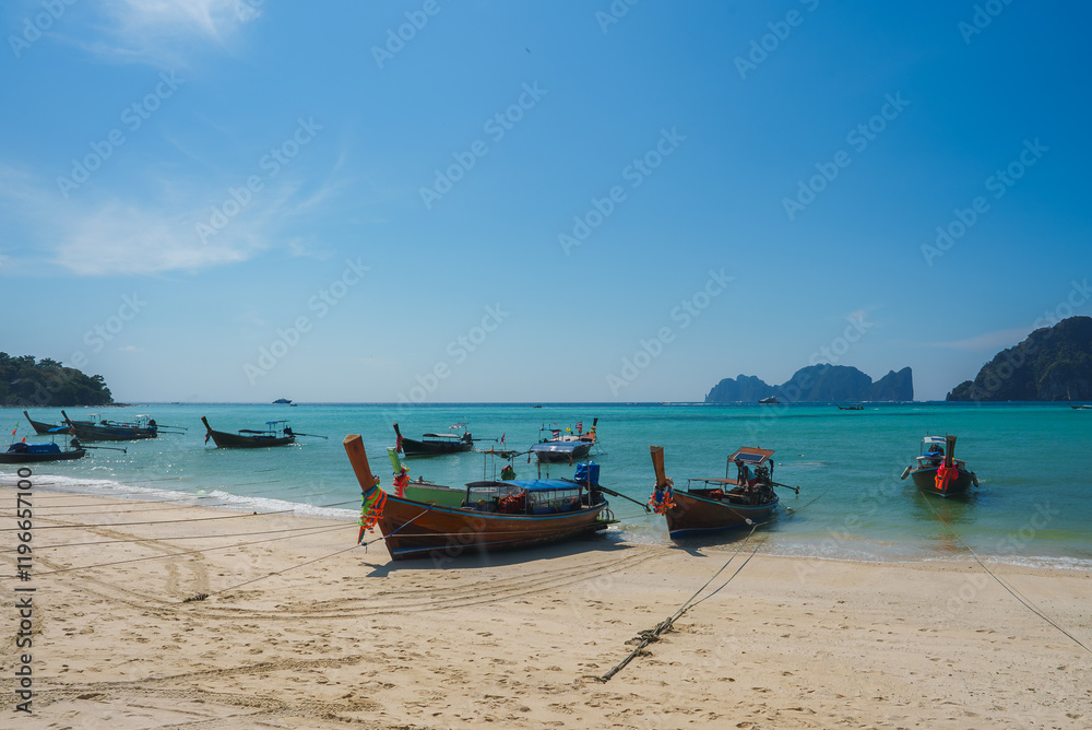 Longtail boats with colorful ribbons rest on a sandy beach in Koh Phi Phi, Thailand, with turquoise water, limestone cliffs, and a clear blue sky. Longtail boats with colorful ribbons rest on a sandy beach in Koh Phi Phi, Thailand, with turquoise water, limestone cliffs, and a clear blue sky.