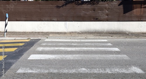 Fence made of white plaster and brown tarpaulin with sidewalk, anti slippery tiles, crosswalk and urban street in front Traffic directional sign on right. Background for copy space. photo