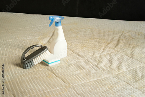 A spray bottle with a sponge and brush on a dirty mattress with yellow stains photo