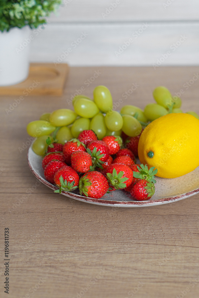 Plate with fresh strawberries, grapes and lemon on the table Plate with fresh strawberries, grapes and lemon on the table