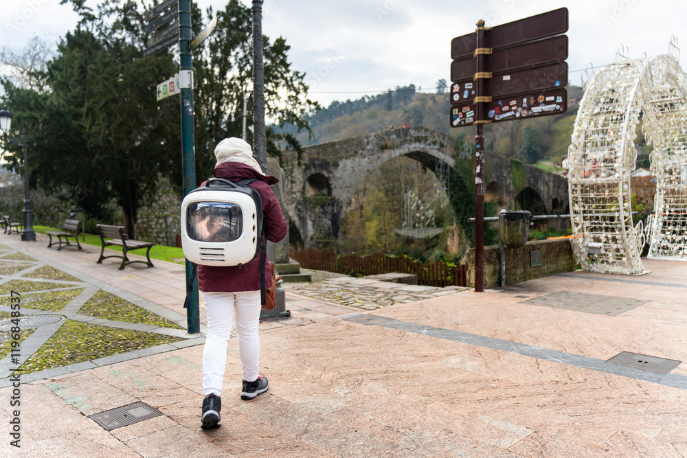 Tourist walking in Asturias, Spain, with his cat on his back in a travel backpack