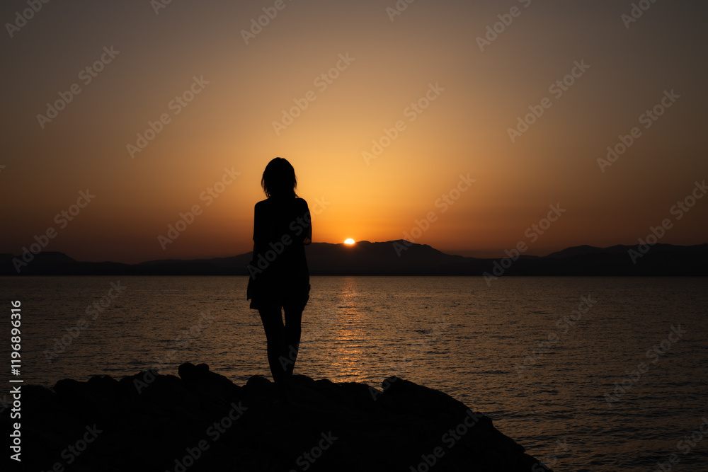 Fototapeta premium Silhouette of a Woman Watching a Peaceful Sunset Over the Sea