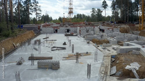 Dolly out above the under-construction foundation of an apartment building under construction, surrounded by a forested area. Top view using a quadcopter.