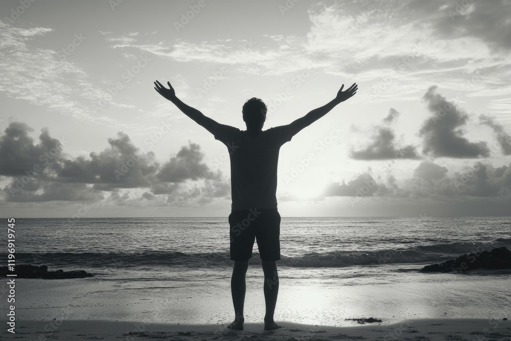 Fototapeta premium Silhouette of a person with arms raised in joy, looking towards the sunset on a beach.