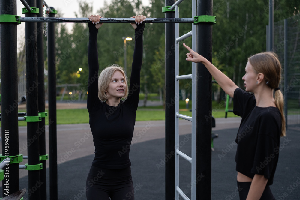 Obraz premium Two happy sporty women working out on outdoor equipment in a summer park. The concept of doing sports with friends