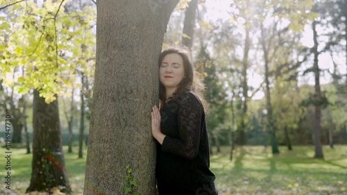 Woman leans with her head against tree in forest on sunny day