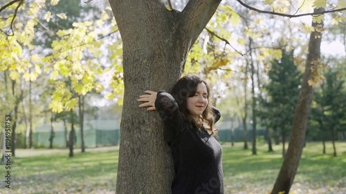 Young woman hugs a tree in a park, smiling and enjoying the moment. Relaxation and mental health conept
