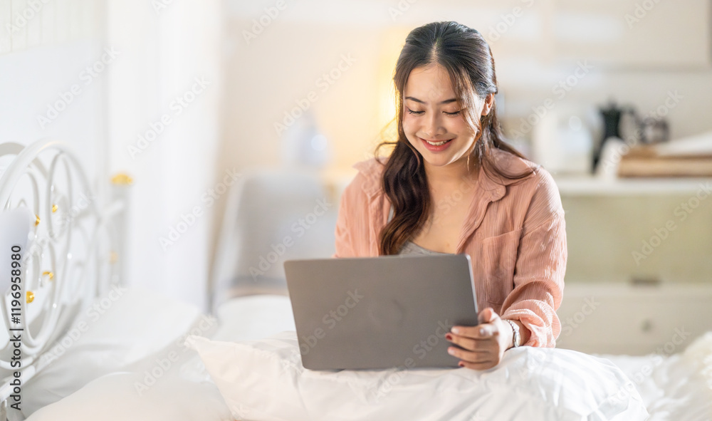 Woman working on a laptop in a cozy bedroom during evening hours while enjoying a relaxed atmosphere Woman working on a laptop in a cozy bedroom during evening hours while enjoying a relaxed atmosphere