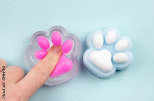 Person finger squeezing cute cat paw shape squishy jelly slime toy, studio shot, copy space. Modern popular sensory toy concept.