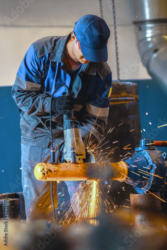 Wallpaper Mural Male worker grinding metal pipe in industrial setting with safety gear. Torontodigital.ca
