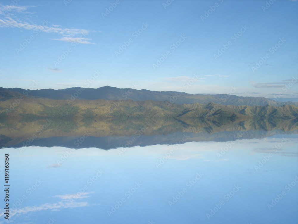 Mountain range reflecting on calm water surface under blue sky Mountain range reflecting on calm water surface under blue sky