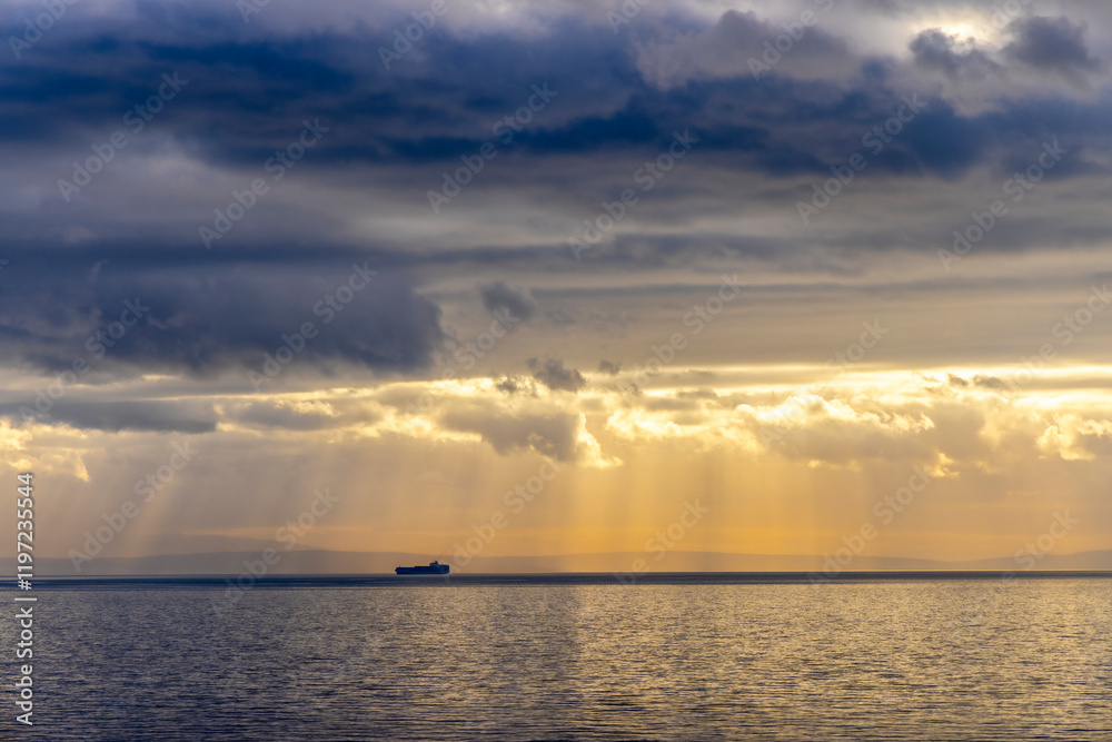 Sun rays peaking through the dark clouds on a ship floating in the adriatic sea creating a dramatic effect