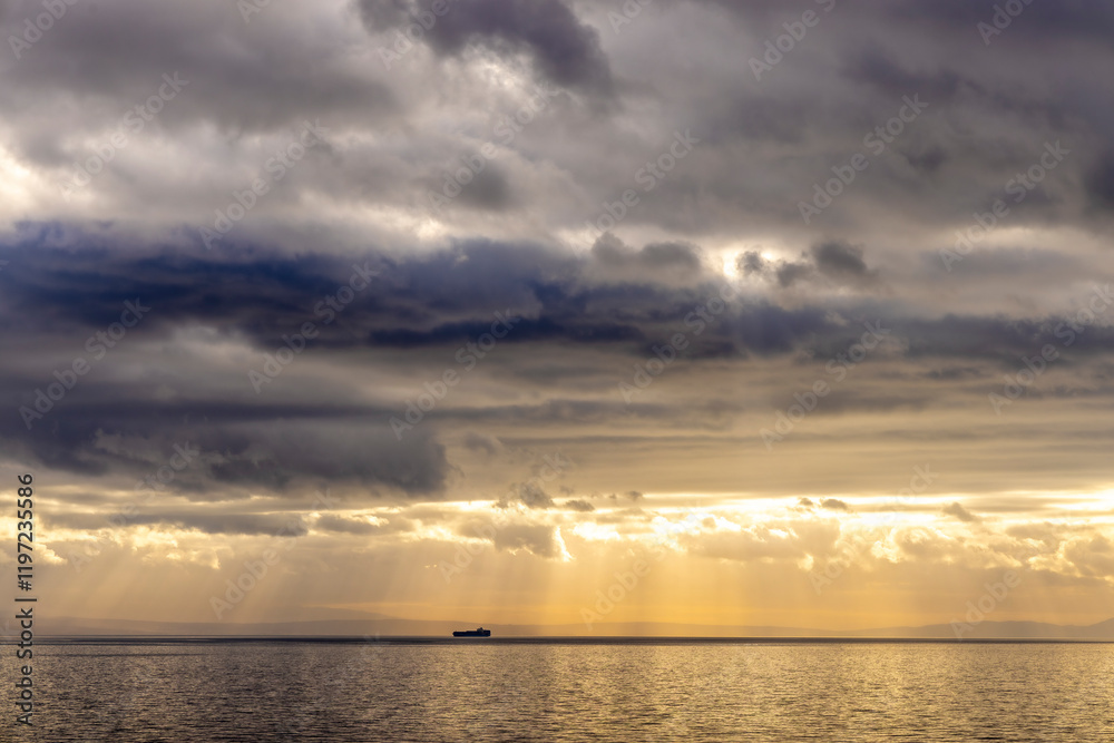 Sun rays peaking through the dark clouds on a ship floating in the adriatic sea creating a dramatic effect