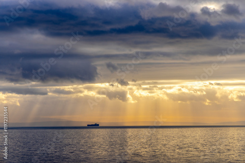 Obraz na płótnie Sun rays peaking through the dark clouds on a ship floating in the adriatic sea creating a dramatic effect w salonie