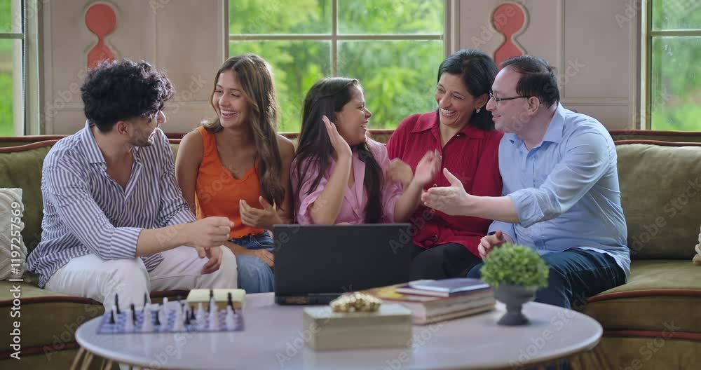 Indian happy young adult multi family group mom dad sitting cozy sofa couch use laptop watch movie film give high five teen girl child male female man boy look show enjoy have fun joy spend day time
