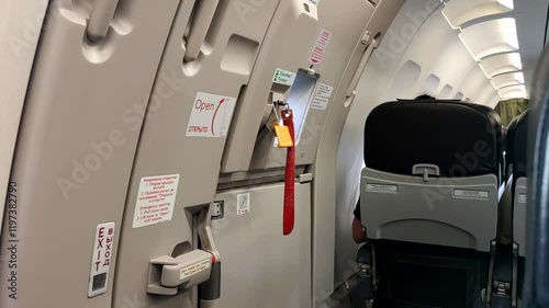 This captures a close-up of the emergency exit door inside an airplane cabin, highlighting safety instructions and seating arrangements while passengers await takeoff.