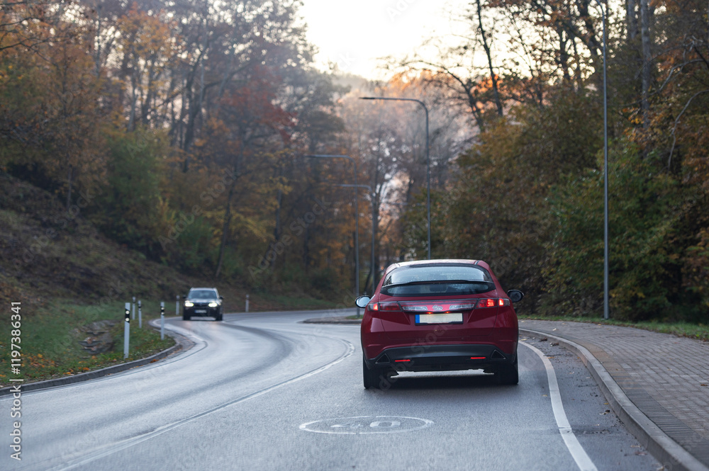 Rear view of a red car on a bend in an autumn road, speed limit sign Rear view of a red car on a bend in an autumn road, speed limit sign