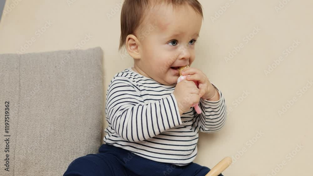 A cheerful baby sits on a couch, curiously exploring a toy with both hands. The child, dressed in a striped shirt and pants, displays excitement during playtime A cheerful baby sits on a couch, curiously exploring a toy with both hands. The child, dressed in a striped shirt and pants, displays excitement during playtime