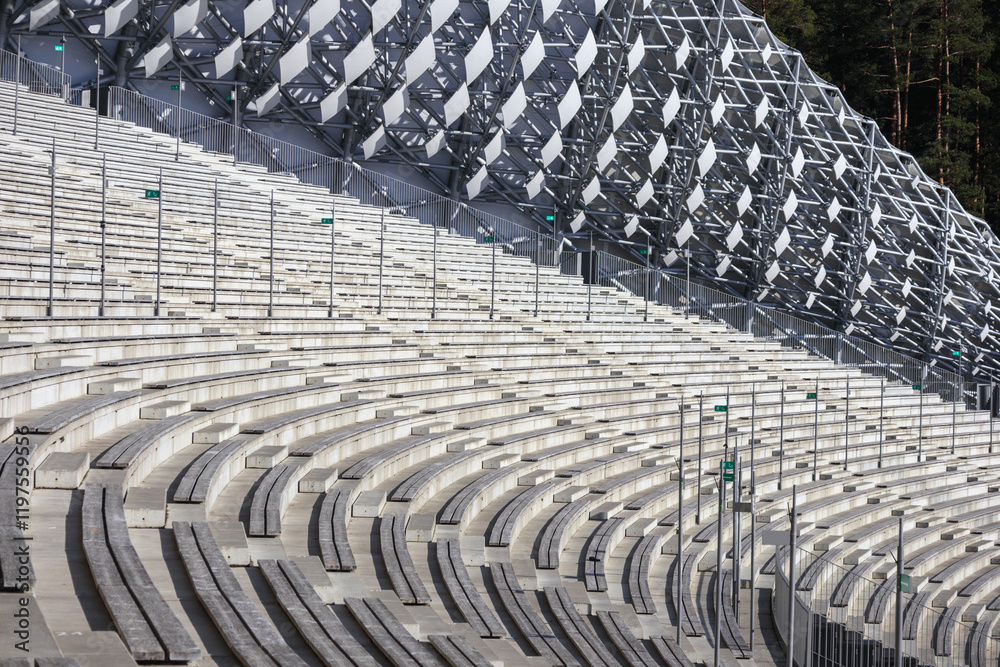 Obraz premium An empty, wooden-seated amphitheater with concrete structures and an unusual geometric screen.