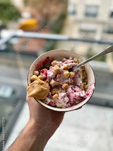 Granola with yogurt, hazelnut and jam in bowl holding in hand peanut butter
