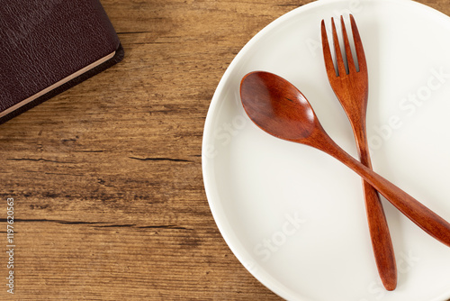 Empty plate with spoon and fork and holy bible book on wooden background. Top view. Christian fasting and spiritual food, biblical concept.
